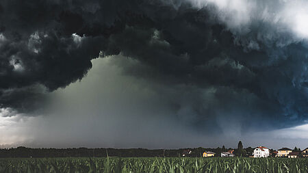 Dunkle, unheilbringende Wolken kündigen einen Sturm an über einem Feld nahe einem Dorf