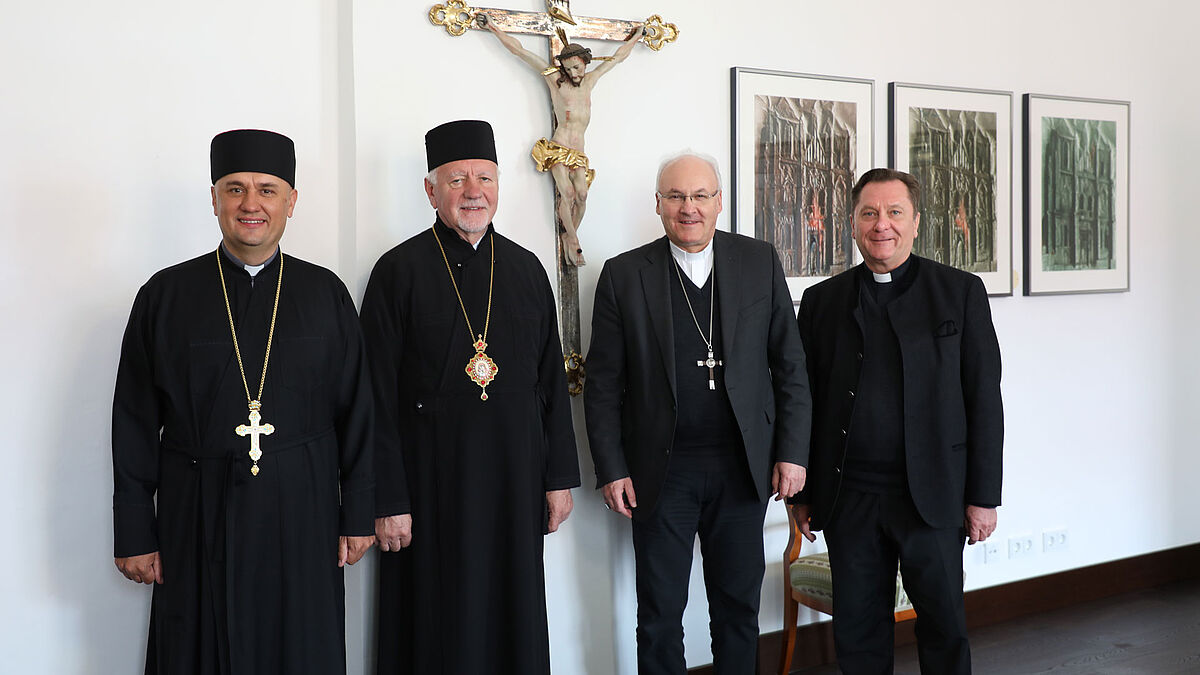 Vier Katholische und ukrainisch-katholische Bischöfe und Priester stehen vor einem Kreuz