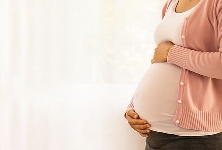 Schwangere Frau hält sich den runden Babybauch